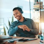 Happy businessman, consultant and laptop with headset for communication or online advice at office. Man, employee or friendly agent talking on computer with smile for virtual assistance at workplace
