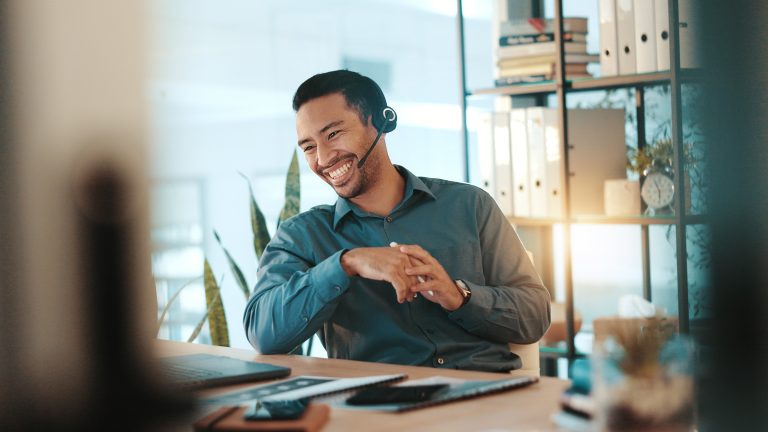 Happy businessman, consultant and laptop with headset for communication or online advice at office. Man, employee or friendly agent talking on computer with smile for virtual assistance at workplace