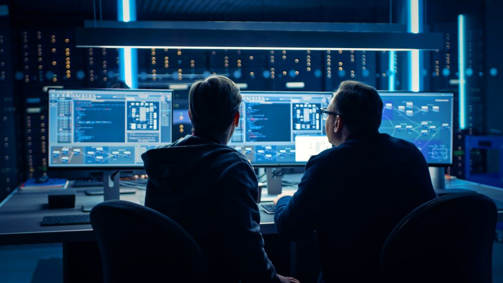 Two Professional IT Programers Discussing Blockchain Data Network Architecture Design and Development Shown on Desktop Computer Display. Working Data Center Technical Department with Server Racks